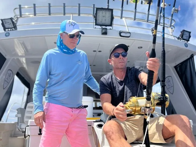 Two anglers on a sportfishing boat actively engaged in reeling in a catch, showcasing the excitement of deep-sea fishing.