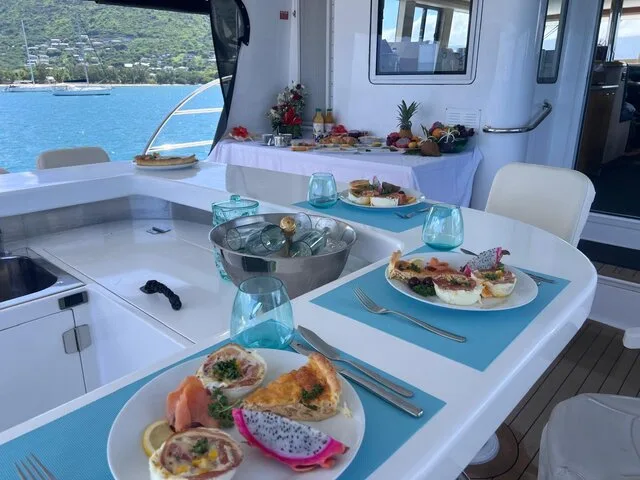 A beautifully arranged dining area inside a luxury boat, featuring gourmet meals and a scenic view of the water and surrounding hills.