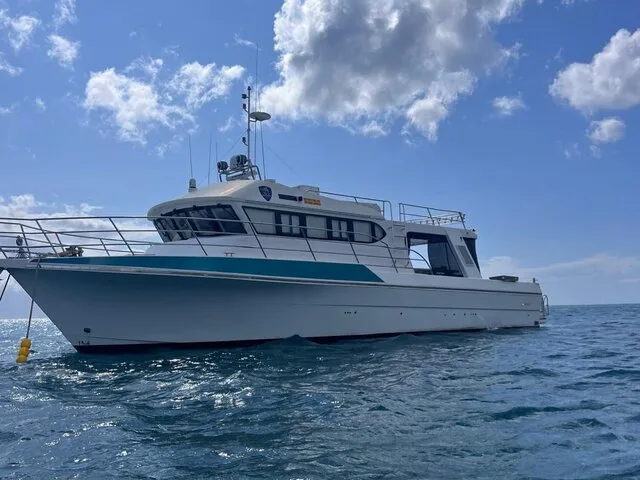A sleek fishing charter boat captured from the side, showcasing its design against a clear blue sky and calm waters.