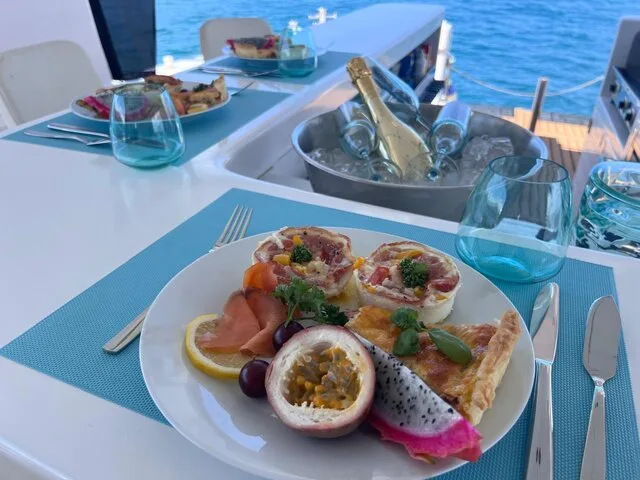 A beautifully arranged meal on a boat, featuring a variety of dishes and drinks, set against a backdrop of the ocean.