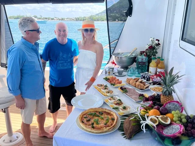Guests enjoying a gourmet spread on a luxury fishing charter, featuring a variety of fresh fruits and pastries against a stunning ocean backdrop.