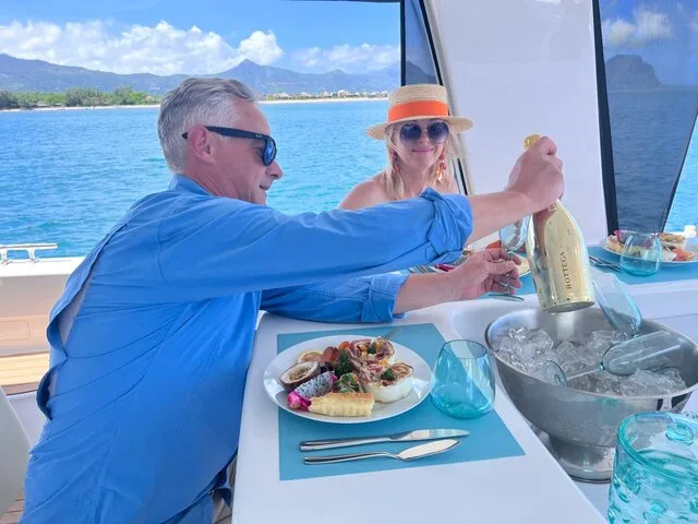 Couple enjoying a luxurious dining experience on a yacht, featuring gourmet food and champagne against a stunning coastal backdrop.