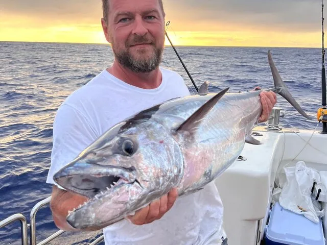 An angler proudly displaying a large Wahoo against a stunning sunset backdrop while fishing offshore.